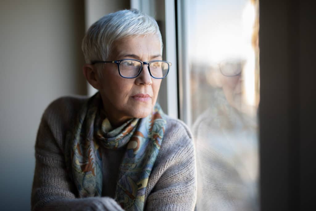 Older woman looking out window pensively