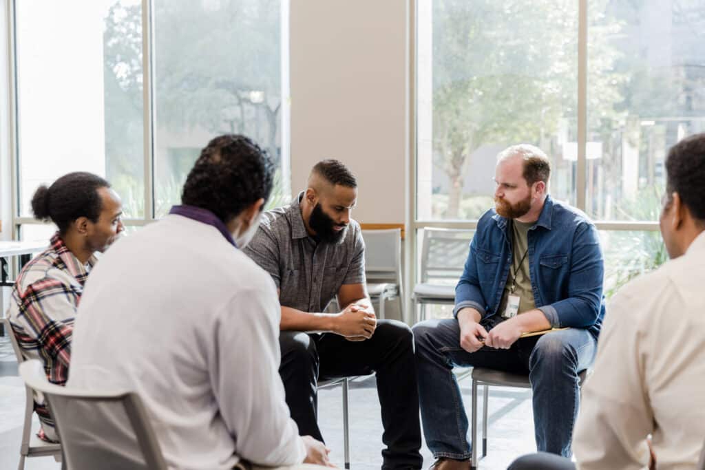 Diverse men sit quietly in support of male friend