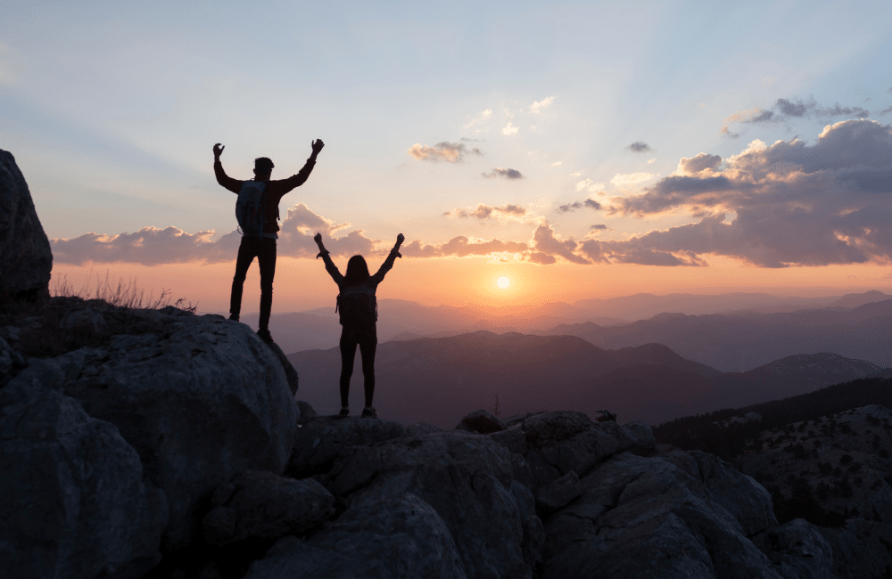 Two people at top of mountain overlooking sunrise