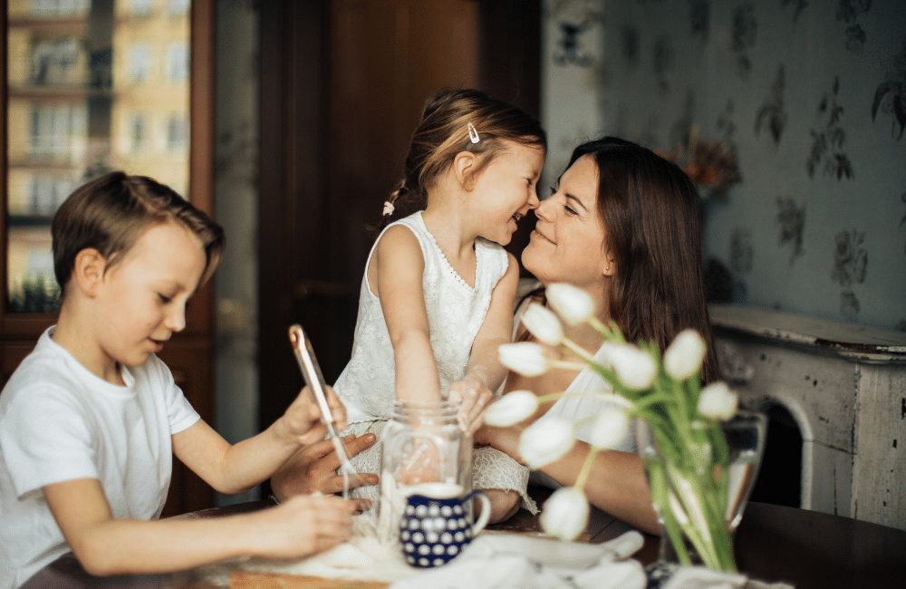 Woman sitting at table with little girl in lap and little boy beside her