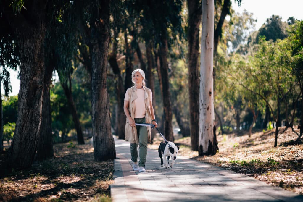 Woman walking a dog along a path through the woods