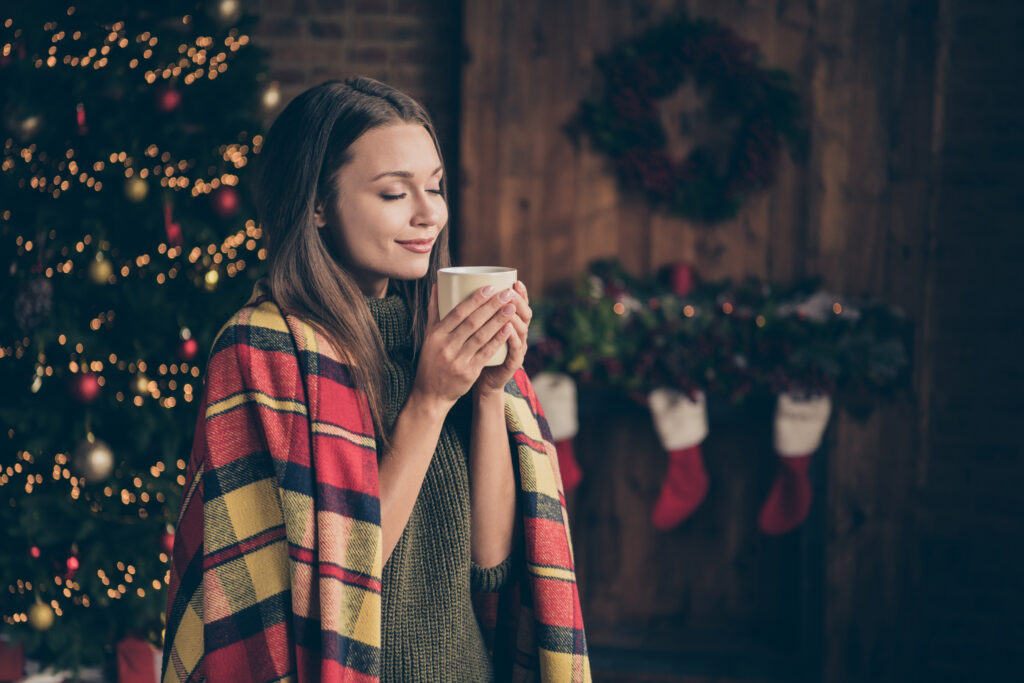 woman with hot beverage smiling in front of holiday scene